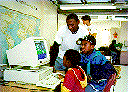 [Photo:  Learn and Serve workers helping school children 
use a computer.]