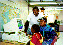 [Photo:  Learn and Serve workers helping school children 
use a computer.]