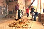 A man wets down the stones of a tile fresco to show off its details, which have dulled from age.